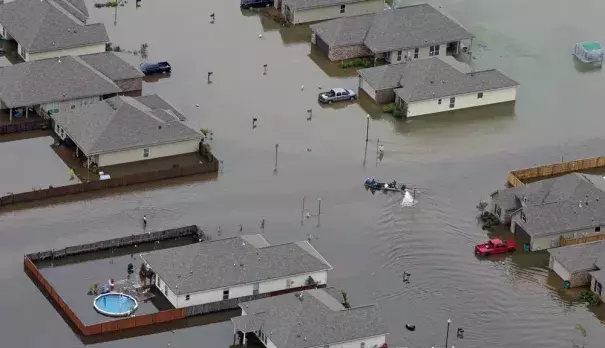 FILE- A boat motors between flooded homes after heavy rains inundating the region, in Hammond, La., on Aug. 13, 2016. A new study Thursday, May 18, 2023, finds the natural burst of El Nino warming that changes weather worldwide is far costlier with longer-lasting expenses than experts had thought, averaging trillions of dollars in damage. (Credit: AP Photo/Max Becherer, File)