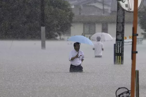 People wade through a street due to a heavy rain in Kurume, Fukuoka prefecture, southern Japan Monday, July 10, 2023. Scientists have long warned that more extreme rainfall is expected in a warming world. (Credit: Kyodo News via AP)